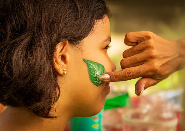 Uma mão pintando uma folha no rosto de uma criança.